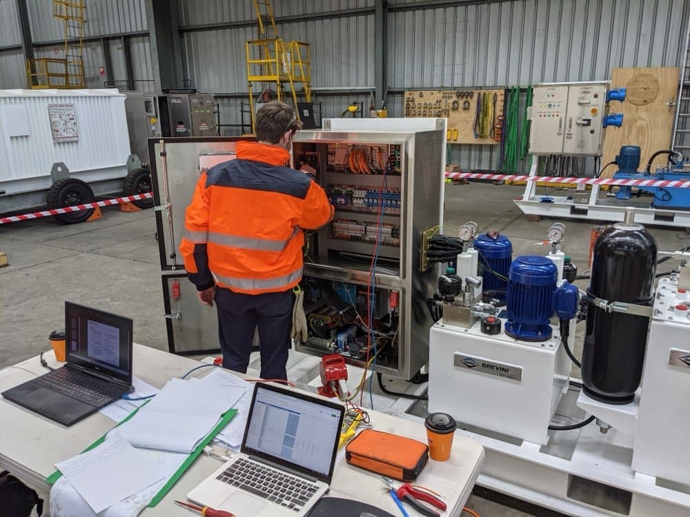 Engineer commissioning a control panel on a hydraulic power unit in a builder's workshop